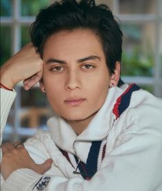 a man with black hair and piercings on his ear wearing a white jacket looking at the camera