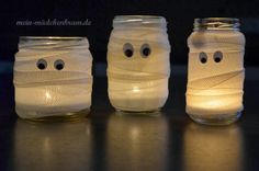 three mason jars with faces and eyes made out of plastic wrapped in white yarn, sitting on a table