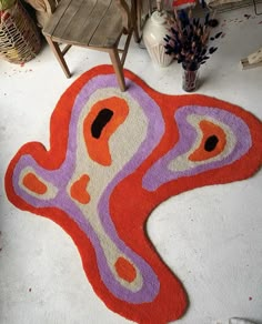 an orange and purple rug on the floor in front of a chair with a plant