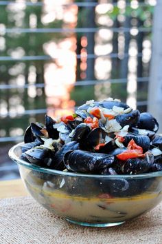 a bowl filled with mussels and vegetables on top of a table next to a window