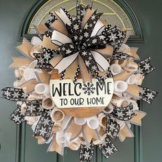 a welcome to our home wreath hanging on the front door with black and white bows