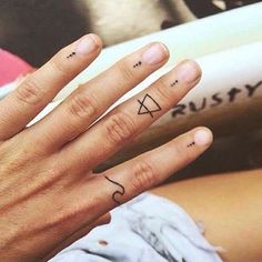 two fingers with small tattoos on them, one has a triangle and the other has a number