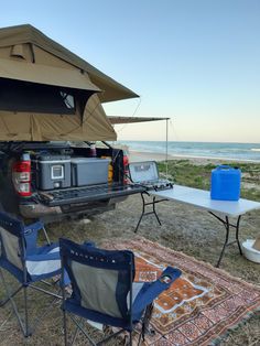 the back end of a truck parked on top of a grass covered field next to an ocean