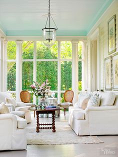 a living room filled with white furniture and lots of windows covered in blue tints