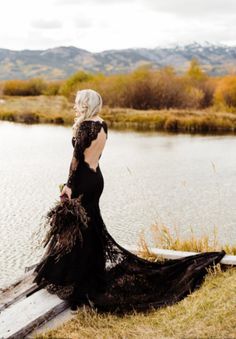 a woman in a long black dress sitting on the edge of a body of water