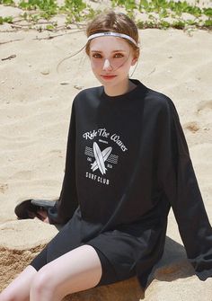 a woman sitting on the sand wearing a black shirt and headband with her legs crossed