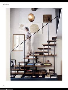 a woman standing on top of a stair case next to a book shelf filled with books