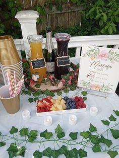 a table topped with plates and cups filled with fruit next to candles on top of a white table cloth