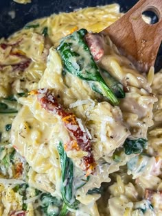 pasta with spinach, chicken and cheese in a skillet being stirred by a wooden spoon