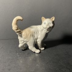 a white cat figurine sitting on top of a black table next to a gray wall