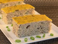 three pieces of food sitting on top of a white plate with green onions next to it