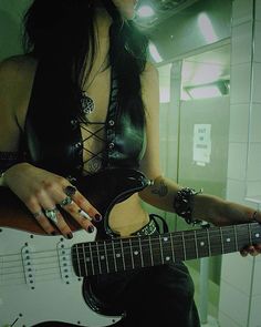 a woman with long black hair is playing an electric guitar in front of a mirror