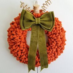 an orange wreath with a green bow hanging on a wall