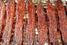 bacon is being grilled on the grill with tongs and seasoning flakes