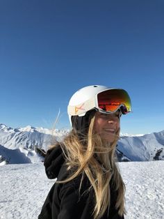 a woman wearing skis and goggles standing on top of a snow covered slope