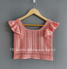 a pink crochet top hanging on a wooden hanger against a gray wall