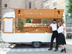 a man and woman standing in front of a food truck with lights on the side