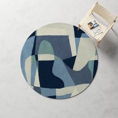 a round rug with an abstract design in blue and grey colors on the floor next to a chair