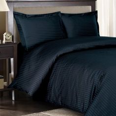 a bed with black comforter and pillows in a room next to a night stand