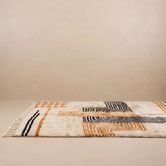 an area rug with different patterns and colors on the floor in front of a beige wall