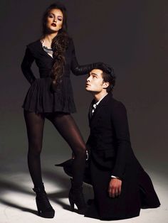 a man sitting next to a woman in a black dress and high heeled boots