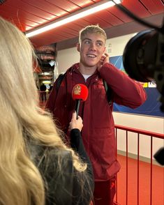 a man in red jacket holding a microphone next to a woman with long blonde hair