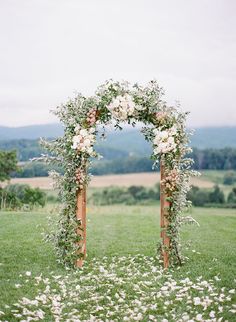 an outdoor wedding ceremony with flowers and greenery on the arch, surrounded by lush green grass