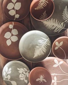 several bowls with designs on them sitting on a wooden table next to another bowl that has leaves painted on it