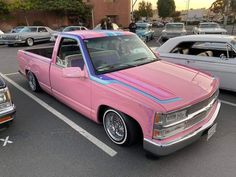 a pink truck parked in a parking lot next to other cars