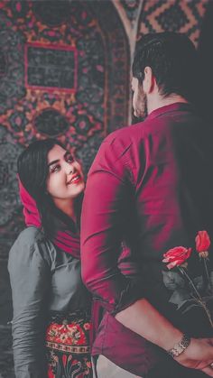 a man and woman standing next to each other in front of a wall with flowers