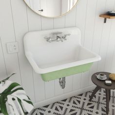 a white sink sitting under a mirror next to a table with a potted plant