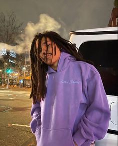 a man with dreadlocks standing in front of a car