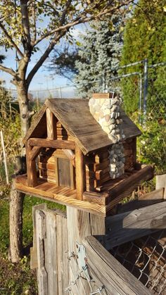 a bird house made out of wood on top of a wooden fence next to a tree