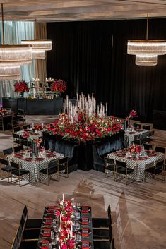 a table set up for an event with red and black flowers on the centerpieces