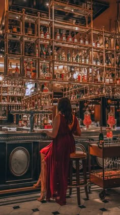 a woman in a red dress sitting at a bar with lots of bottles on the wall