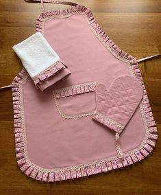 a pink apron and two white towels on a wooden floor with a pair of scissors