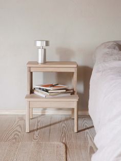 a nightstand with two books on it next to a bed