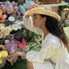 a woman sitting on the ground in front of a bunch of flowers wearing a straw hat