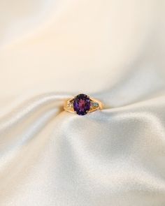 a close up view of a ring with a purple stone in the center on a white fabric