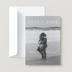 save the date card with an image of a couple hugging on the beach in black and white