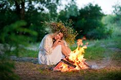 a woman sitting next to a fire in the woods