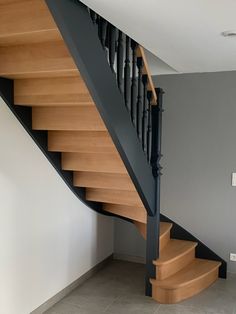 a wooden staircase with black handrails in a room that has gray walls and tile flooring