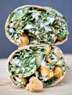 two wraps filled with greens and chicken on top of a wooden table