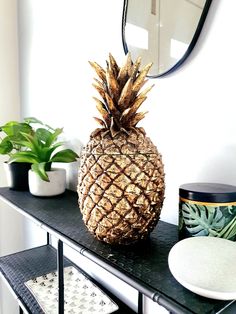 a pineapple sitting on top of a black table next to potted plants and a mirror