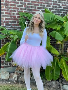 a woman in a pink tutu and tiara standing next to a brick wall