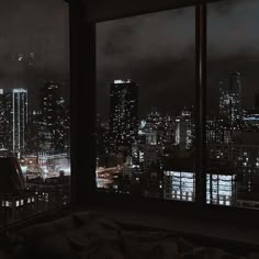 a view of the city at night from a bedroom in a skyscraper building, looking out over a large city