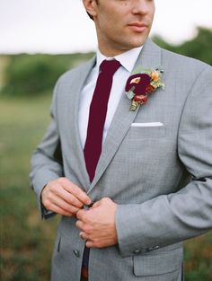 a man in a gray suit with a red tie and flower boutonniere