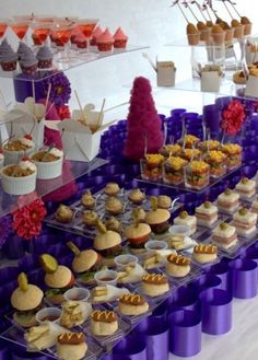 an assortment of desserts are displayed on purple plastic trays and under glass shelves