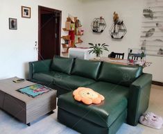 a living room with green leather couches and an animal pillow on the coffee table