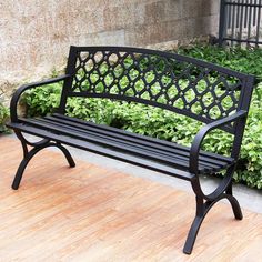 a black bench sitting on top of a hard wood floor next to bushes and shrubbery